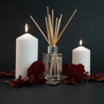 A serene setup of white candles, aromatic diffuser, and floral decor on a dark background.